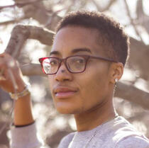 A portrait/headshot of Leo, set outdoors with a blurred background of flowering trees.